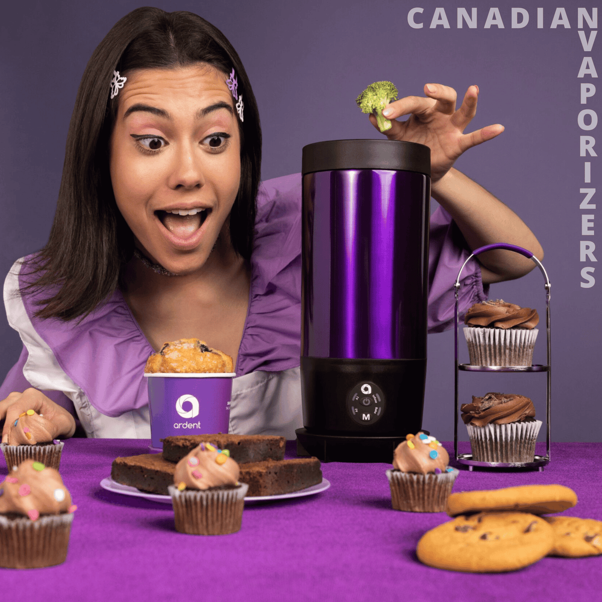 Ardent FX - Purple Ardent FX blender with a tall metallic pitcher, black base, and clear lid beside a woman and decorated cupcakes.